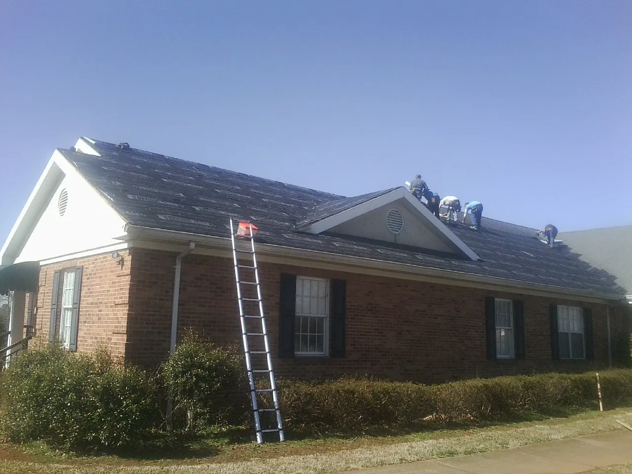 Crew tearing shingles off a brick ranch roof with a ladder set — Emergency Roof Repair work by our crew in Sherborn