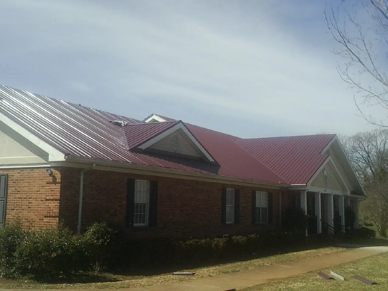 Red metal roof with gabled entries on a long brick building, from a Hail Damage Roof Repair job in Sherborn