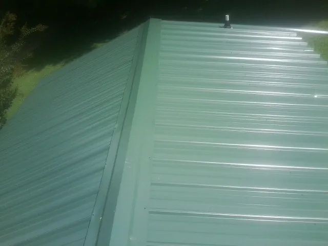 New green metal panels meeting at the ridge of a roof — Flat Roof Repair work by our crew in Sherborn