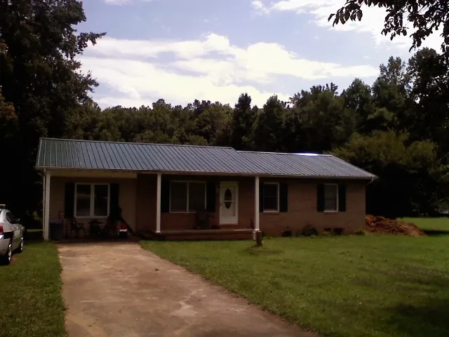 Dark green metal roof on a brick ranch with a covered porch in Sherborn