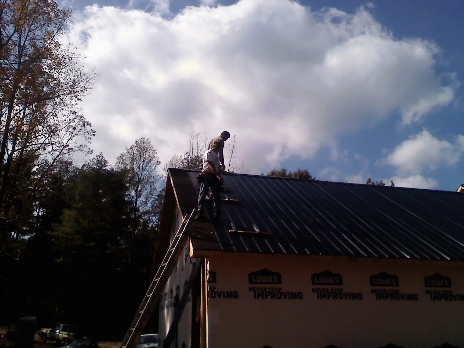 Roofer fastening dark metal panels high against a cloudy sky, from a Roof Inspection job in Sherborn