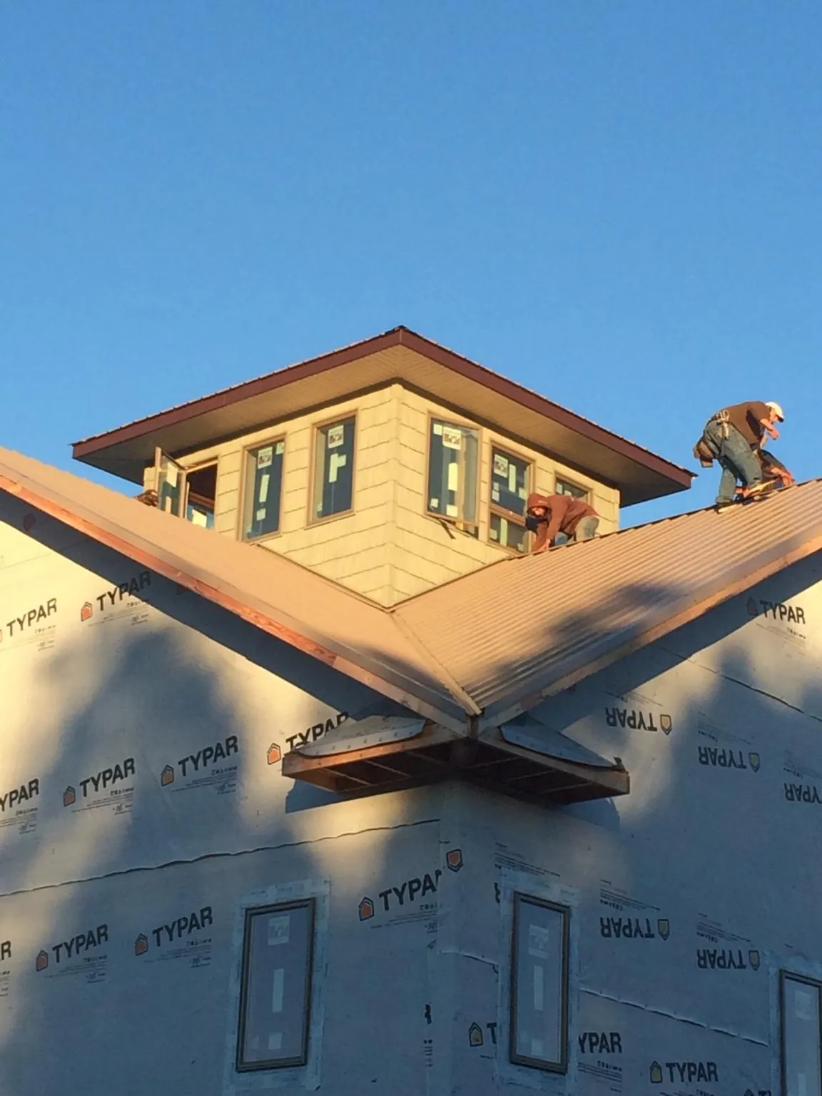 Roofers working around a rooftop cupola on a new metal roof at sunset — Roof Waterproofing in Sherborn by Roofing Brothers